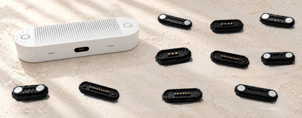 Original waterproof speaker with three dock contacts and all ten original magnetic connector bodies on pale limestone.