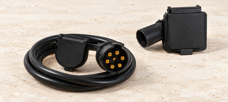 Original rugged vehicle socket and complete coiled seven-contact connector cable on pale limestone.